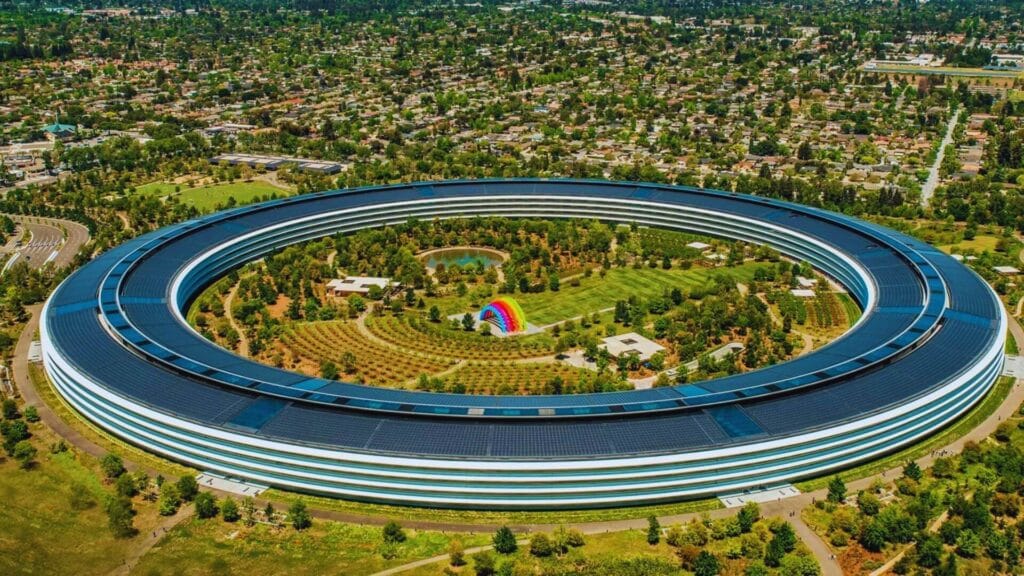 مقر شركة Apple الرئيسي (Apple Park) في مدينة كوبرتينو، كاليفورنيا، بتصميم دائري ضخم يُعرف باسم The Ring، محاط بمساحات خضراء واسعة ويعكس التزام آبل بالابتكار والاستدامة والتقنية المتقدمة.