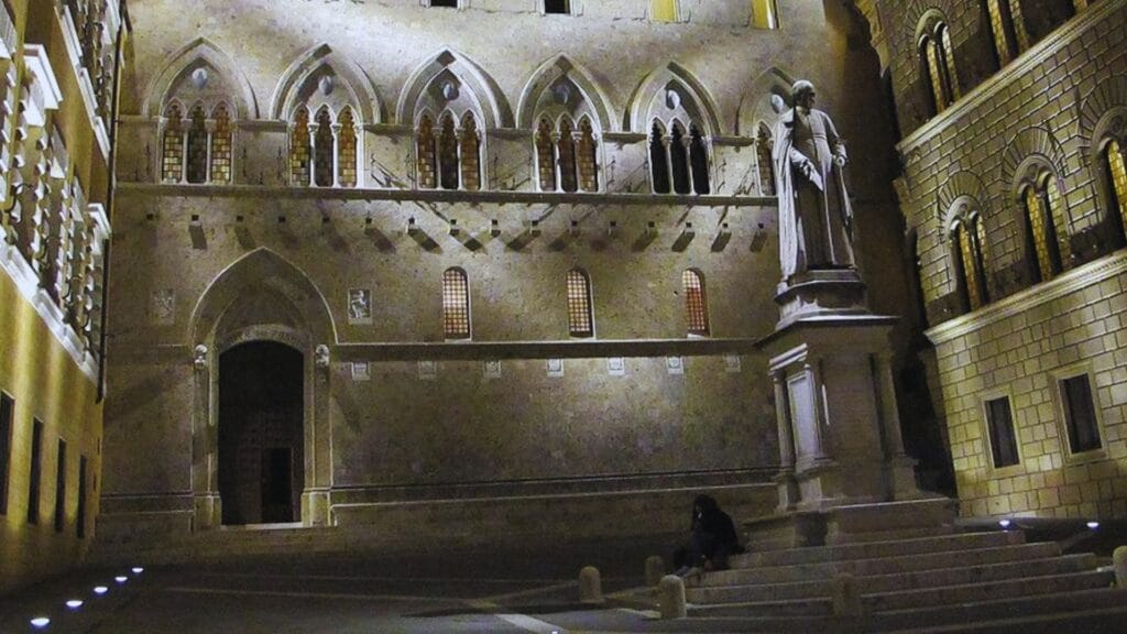 الواجهة التاريخية لقصر ساليمبيني في مدينة سيينا الإيطالية، المقر الرئيسي لبنك مونتي دي باشي دي سيينا، أقدم بنك لا يزال يعمل في العالم، بطراز معماري قوطي وإضاءة ليلية.