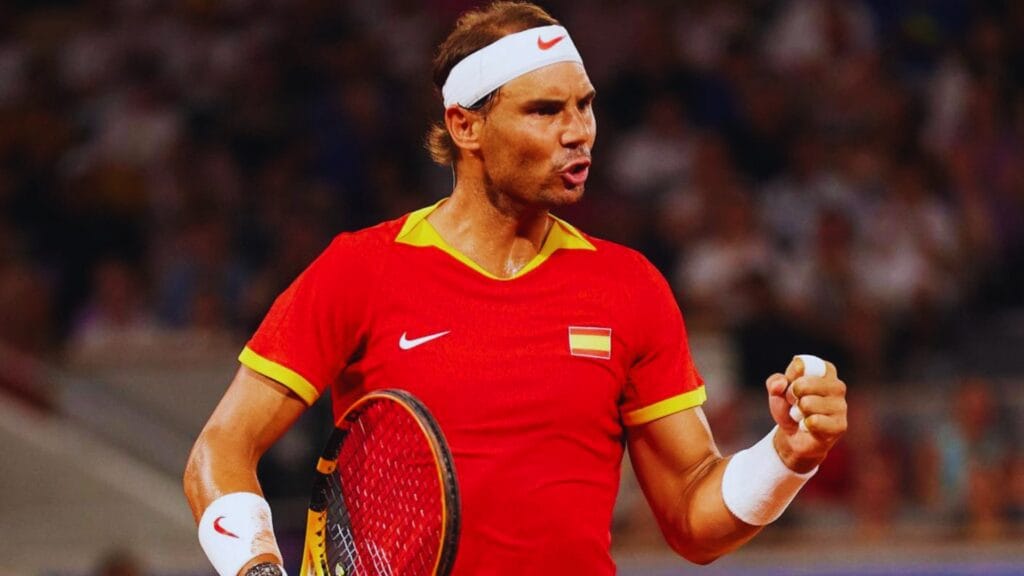 رافايل نادال لاعب التنس الإسباني الشهير خلال مباراة حماسية، مرتديًا قميص منتخب إسبانيا الأحمر مع عصابة رأس بيضاء، يظهر تركيزه وقوته أثناء التنس. نادال يُعد من أفضل لاعبي التنس في التاريخ، حائز على العديد من البطولات الكبرى مثل رولان غاروس وويمبلدون، ويشتهر بأسلوب لعبه الهجومي والمثابرة على الملعب.