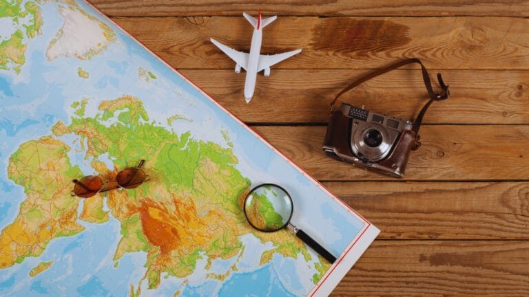 صورة تعبر عن حالة واستعداد للسفر حيث يتواجد بها طائرة صغيرة بجانب خارطة وكاميرا وعدسة مكبرة.