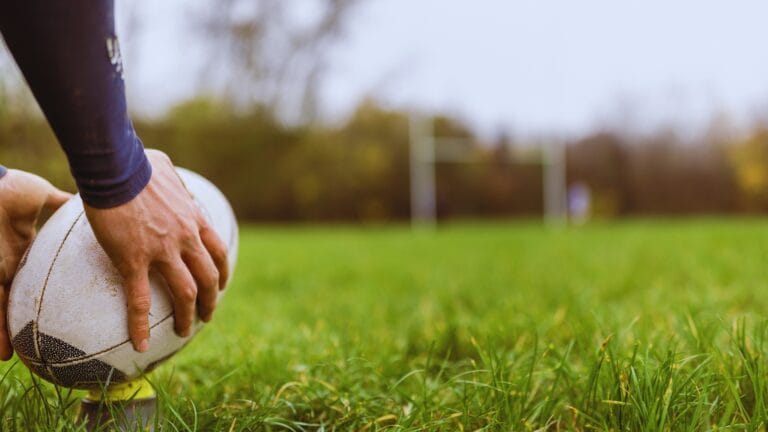 لاعب يمسك كرة الرغبي على أرض ملعب عشبي استعدادًا لبدء المباراة.