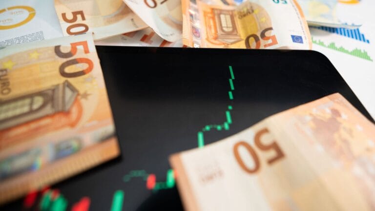 أوراق نقدية من فئة 50 يورو متناثرة حول شاشة لوحية تعرض رسماً بيانياً صاعداً باللون الأخضر، تعبيراً عن نمو المال ومفهوم الاستثمار الناجح.